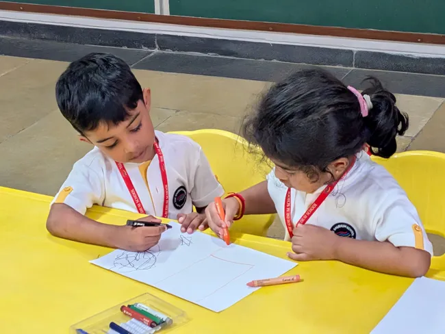 Two primary students drawing together at a yellow table